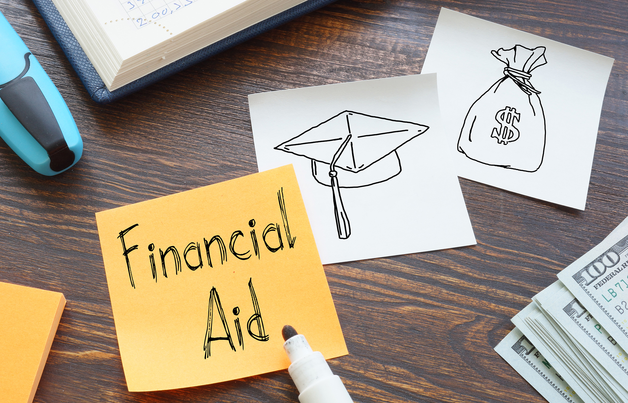 yellow sticky on a desk with the words financial aid in marker