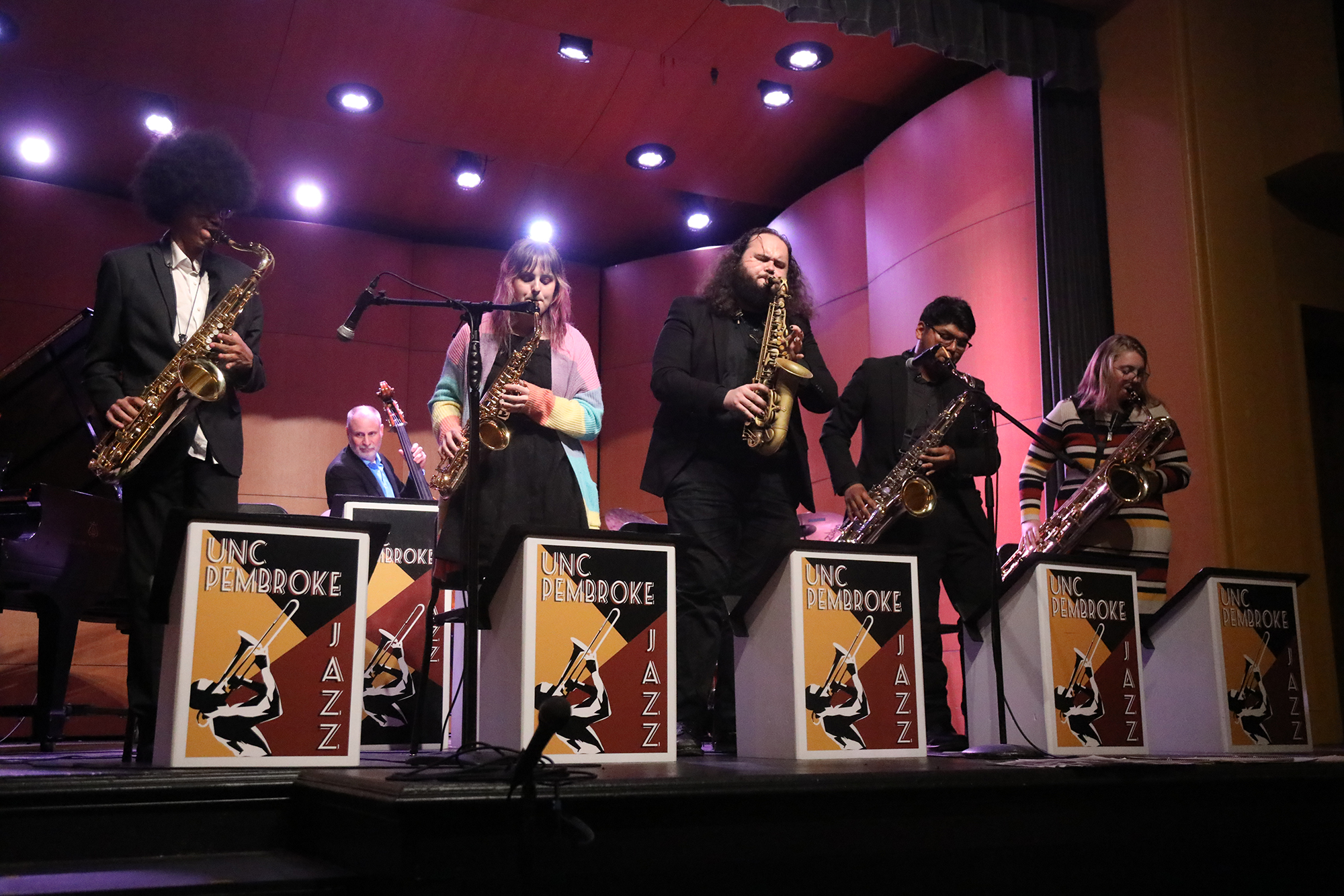 members of the UNCP jazz ensemble playing wind and brass instruments on a lit stage