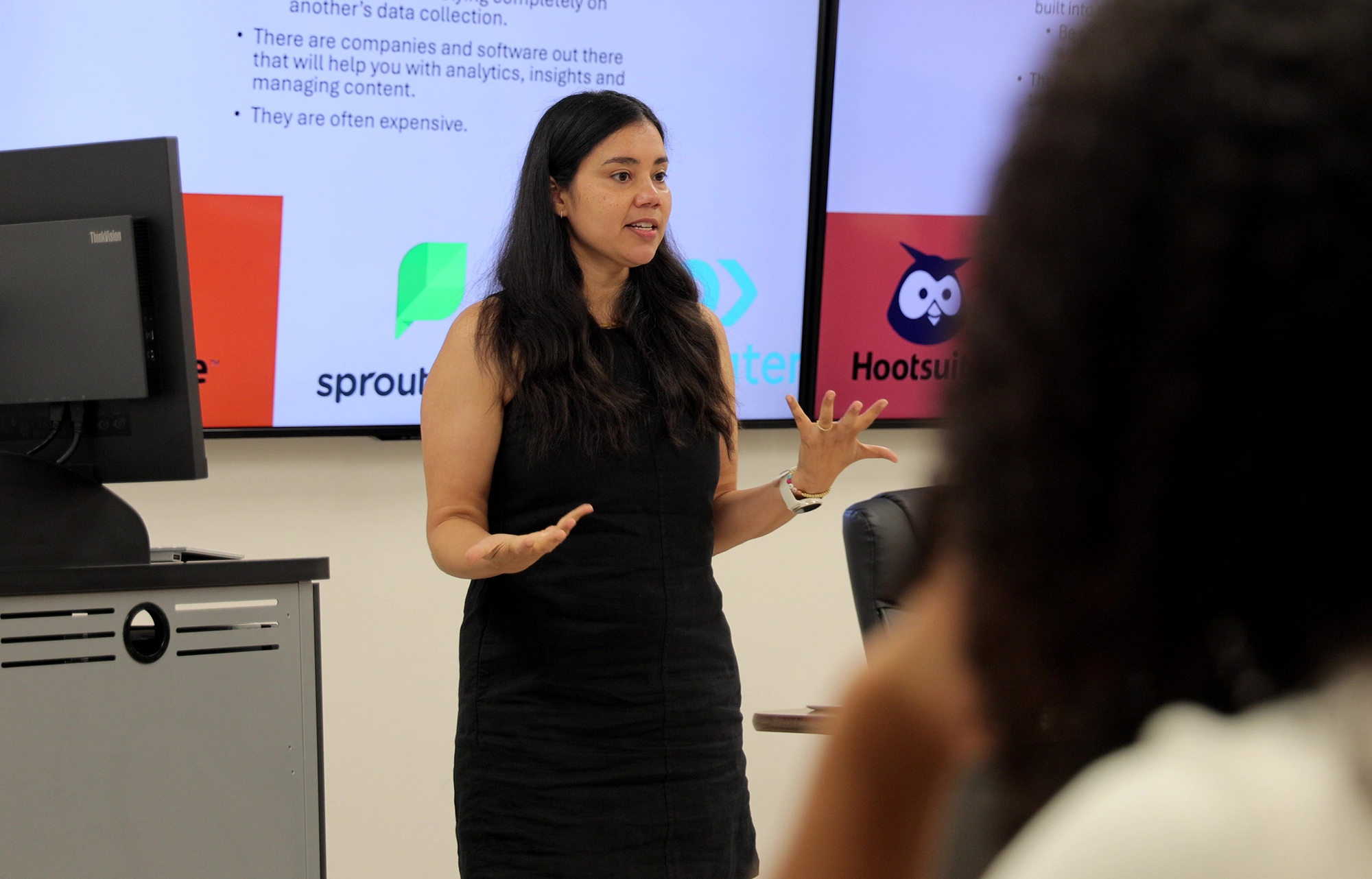 Dr. Emelia Bak teaching public relations at UNC Pembroke, as it relates to shaping perceptions through social media. Dr. Bak stands in front of a large monitor displaying information about various social media tools.