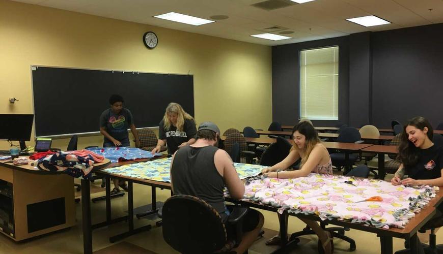 Psi Chi students volunteering to make blankets for the Child Advocacy Center in Fayetteville. We donated 10 blankets and had a lot of fun making them! :-) One of the pictures was taken at the Child Advocacy Center once Babs dropped the blankets off.