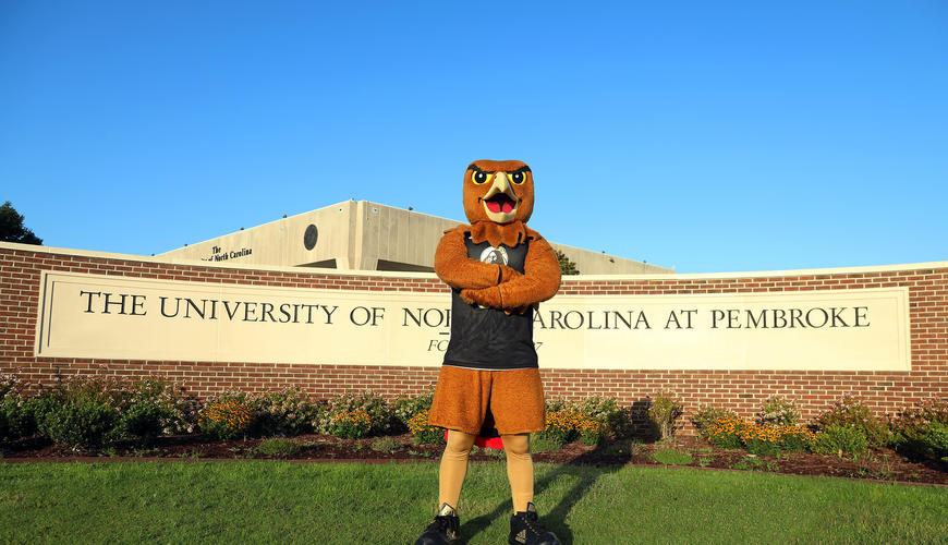 Brave Hawk mascot in front of UNCP main entrance sign