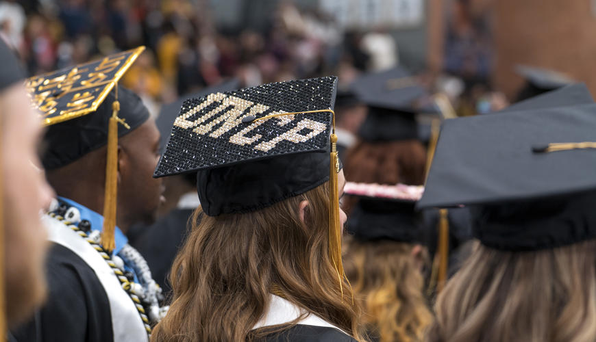 Student sitting at graduation with bedazzled UNCP cap
