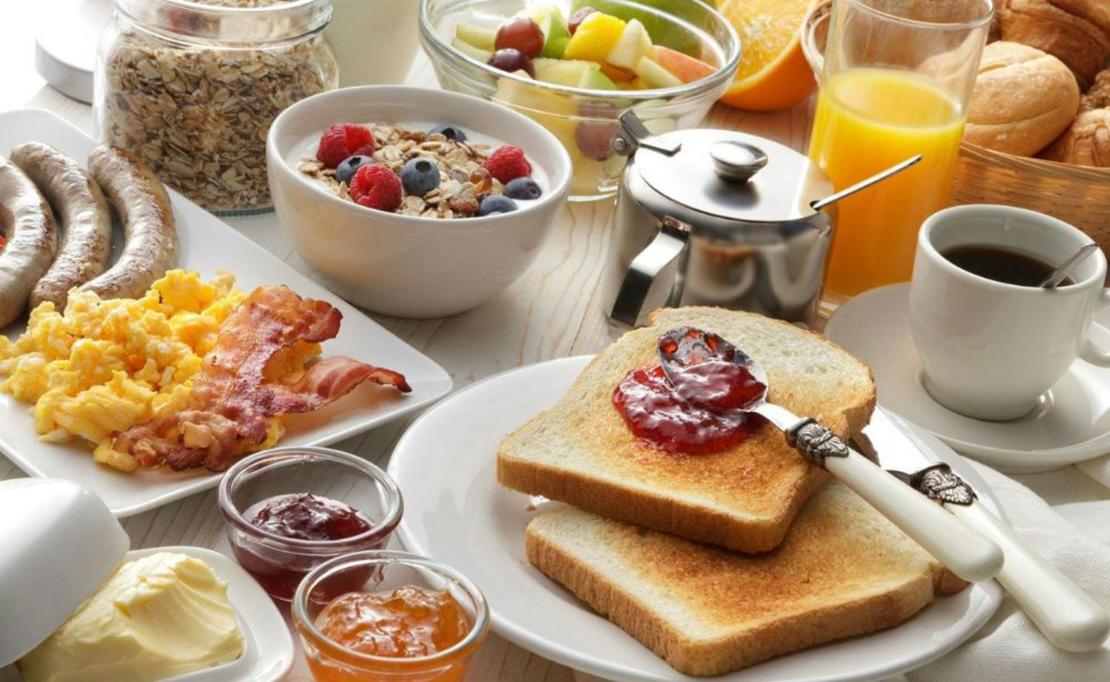 A breakfast spread with toast & grape jelly, orange juice, coffee, oatmeal with fruit, scrambled eggs, bacon, sausage, fruit, milk, and muffins