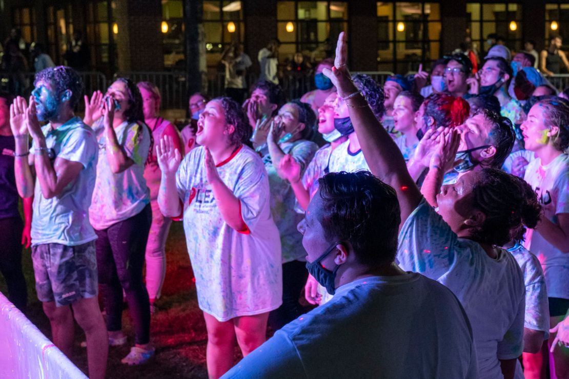 A group of students cheering with their arms up at a dance party with colored lights