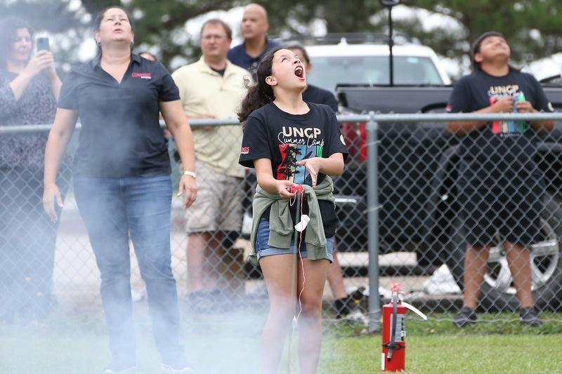 Student and spectators staring into the sky, just after a small rocket has launched.