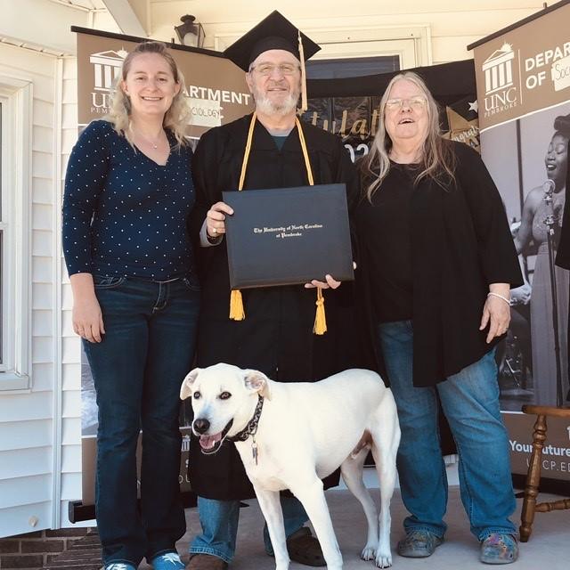 UNCP graduate Eugene Kaplan celebrates during an at-home graduation ceremony with his wife, Glenna, and their daughter, Meggan Hollis