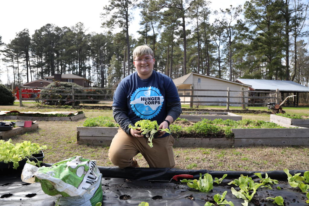 student sits at garden planting lettuce