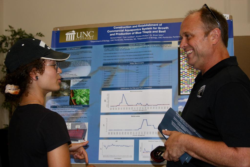 Dr. Bryan Sales (right) chats with a student in front of his students' research poster