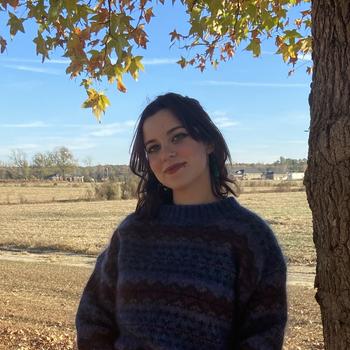 Smiling person in sweater by a tree