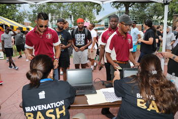 Students checking in to BraveNation Bash at a table with two staff members taking Braves Cards, with a crowd of students waiting in line to sign in. 