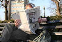 Man, reading newspaper on a park bench.